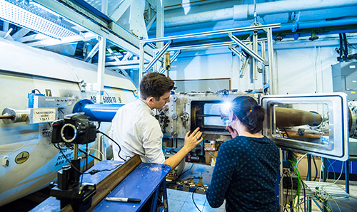 Two students, backs to camera, in front of open machine, discussing its contents